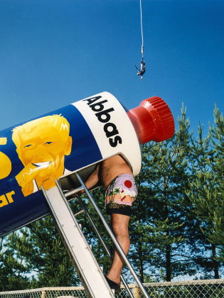 Man i badshorts klättrar in i en jättetub med Kalles kaviar-design; kvinna står bredvid, person bungyhoppar i bakgrunden.