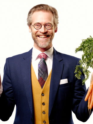 Henrik Widegren med en varmkorv i bröd i ena handen och ett knippe morötter i den andra handen.