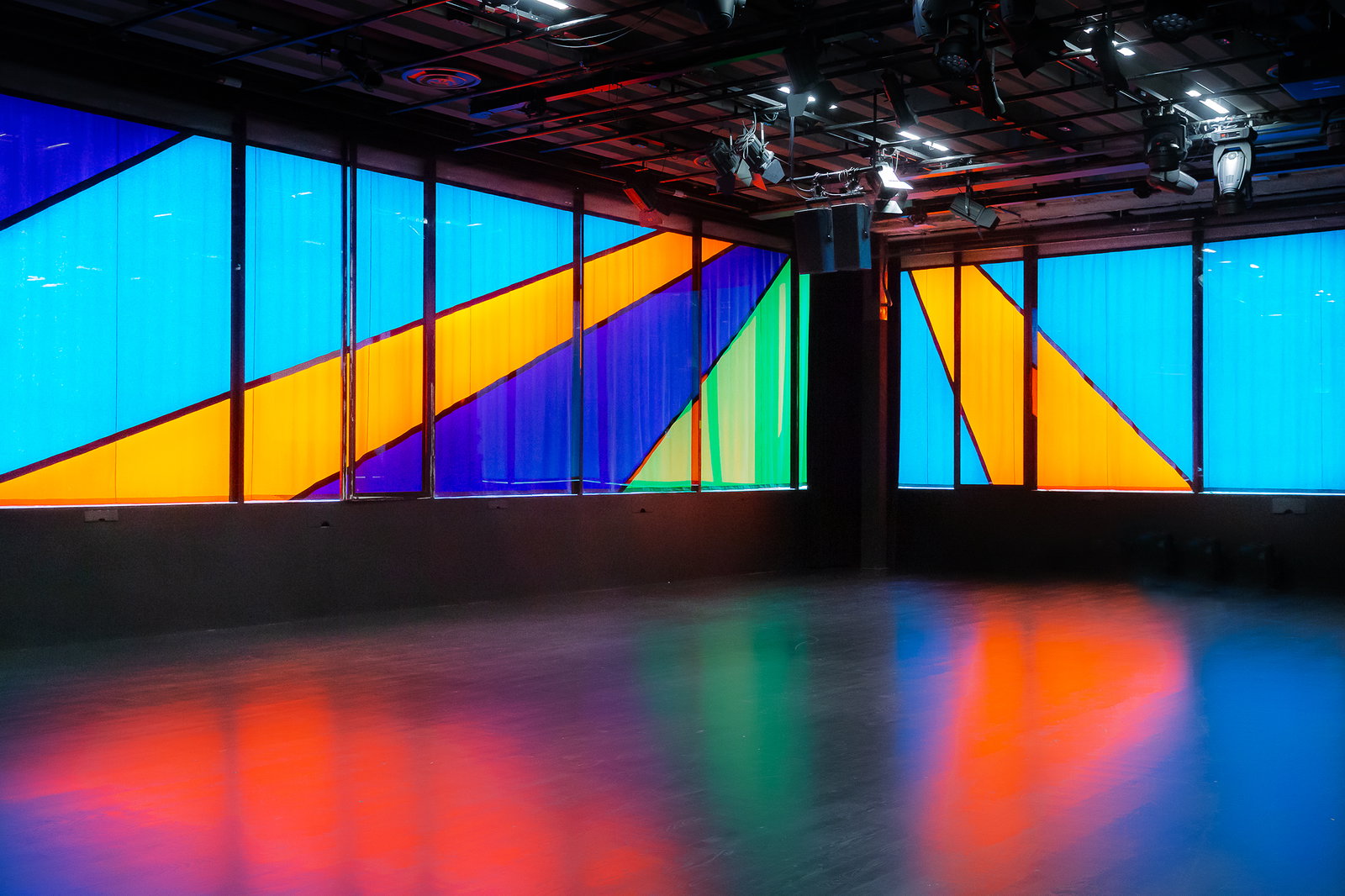 Ett draperi i olika färger framför stora fönster. 