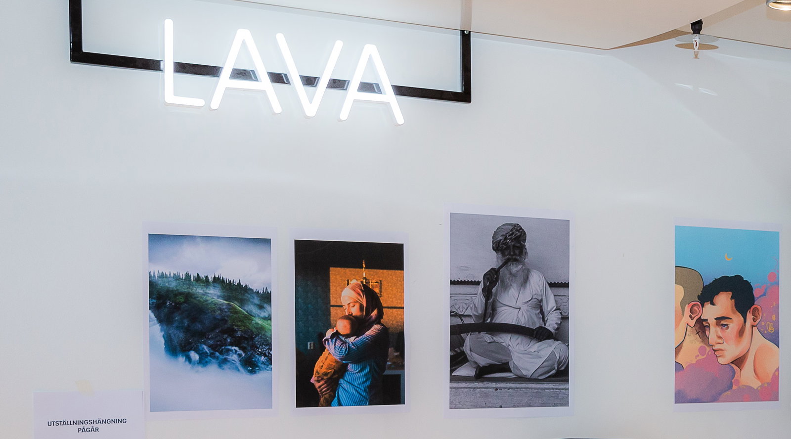 Tavlor uppsatta på en vägg samt en skylt där det står Lava. 