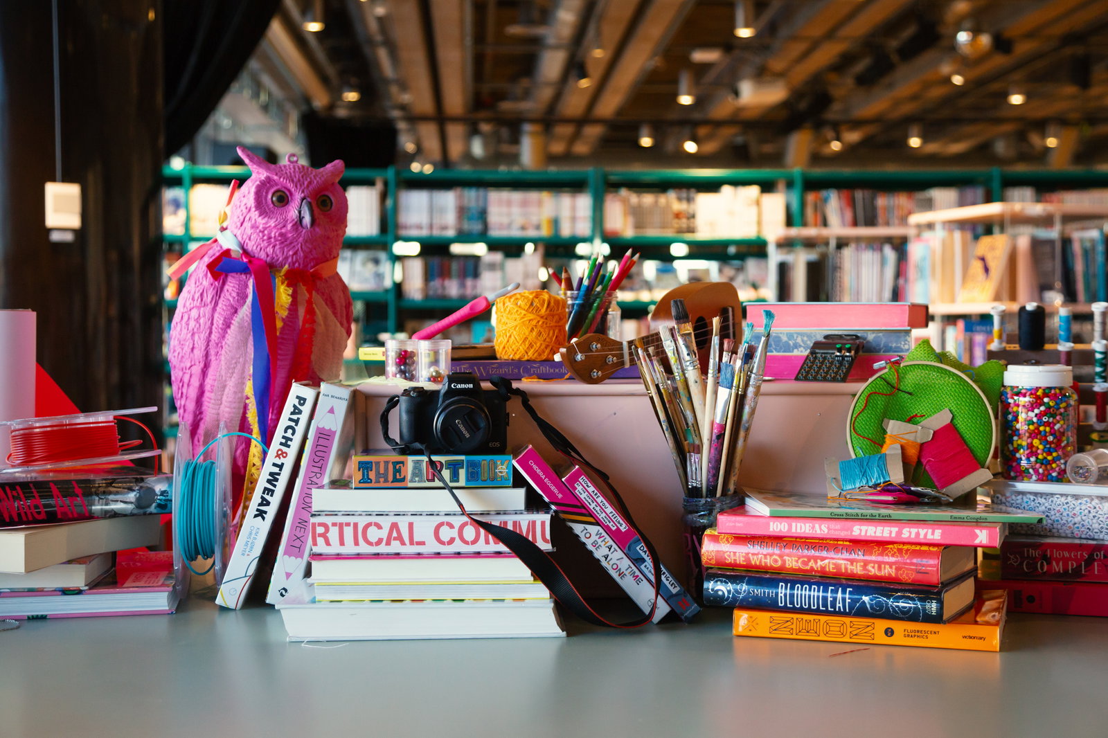 Bord med konstmaterial som penslar, garn, kamera och staplade böcker i färgglada omslag.