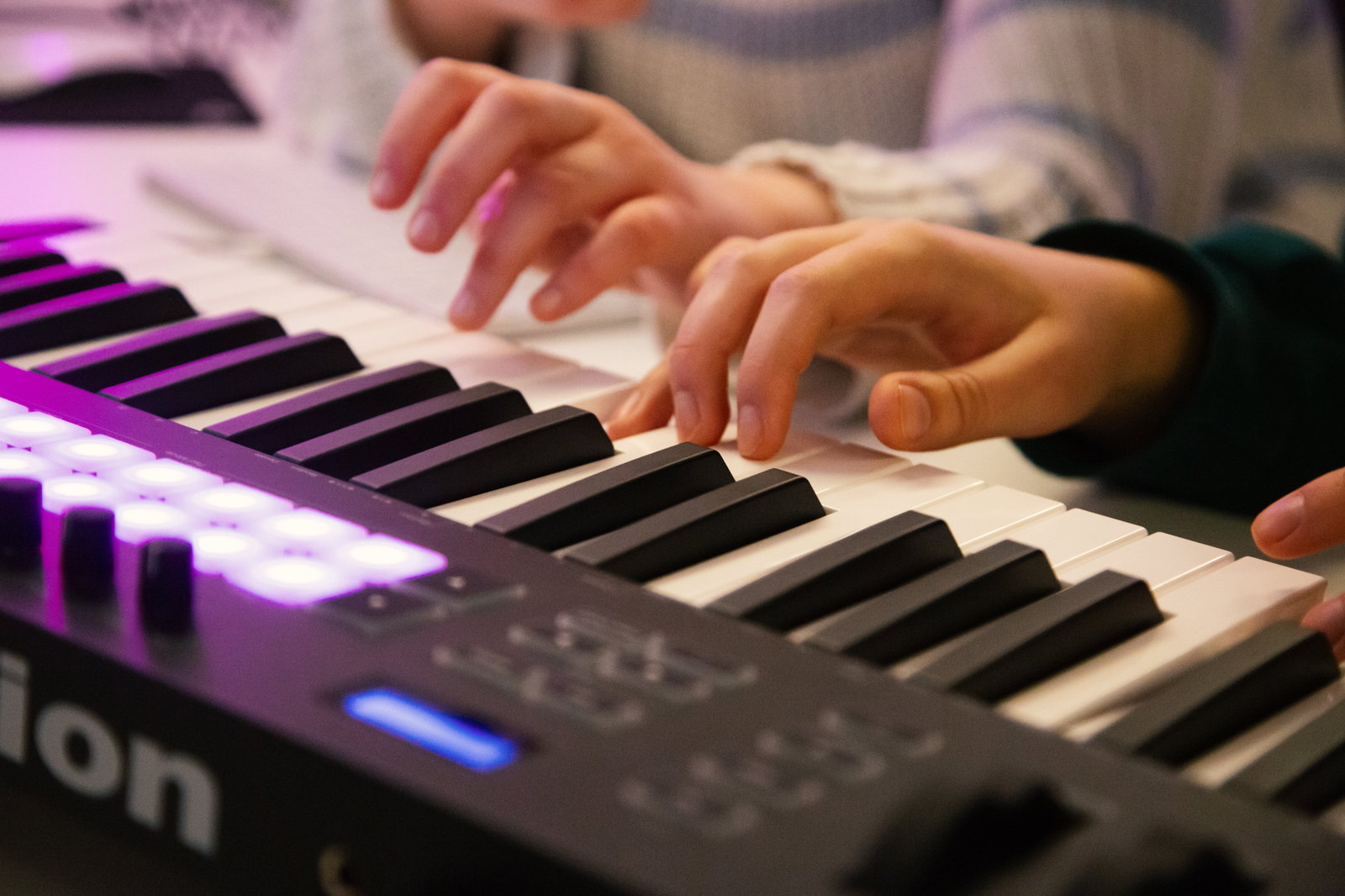 Två personer spelar på ett digitalt piano, med fokus på deras händer på tangenterna.