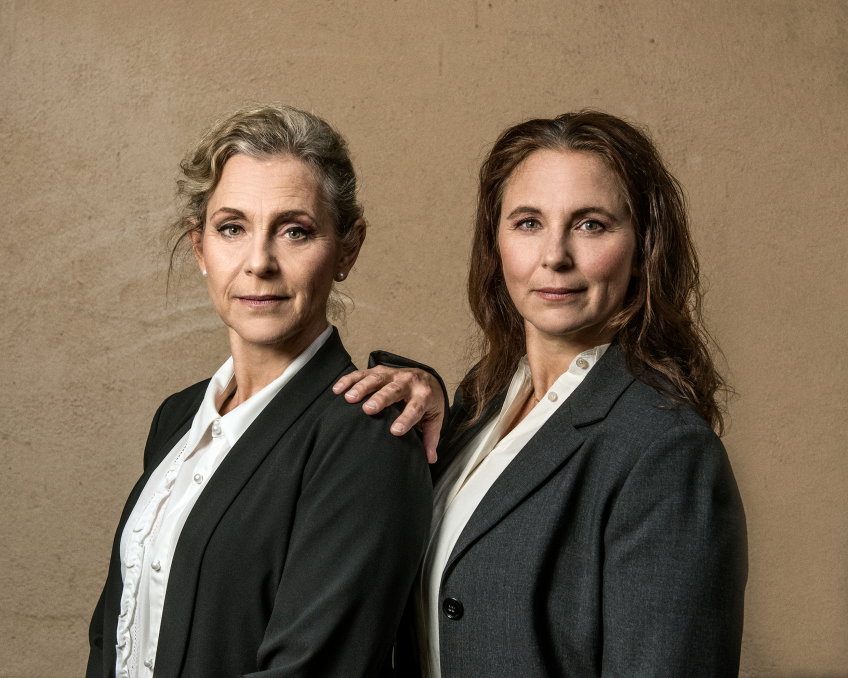 Helen Sjöholm och Anna Fahlsteddt i svarta kavajer fotade mot en gul vägg.