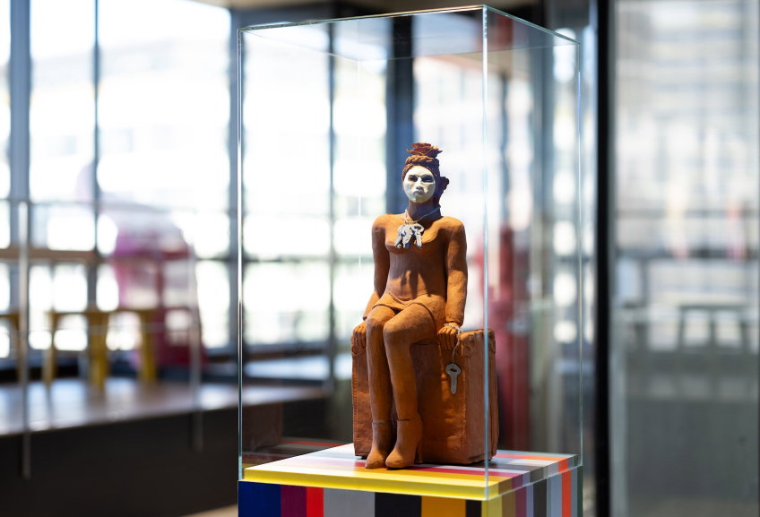 Närbild av keramisk figur med vitmålat ansikte och smycke, placerad i en glasmonter.