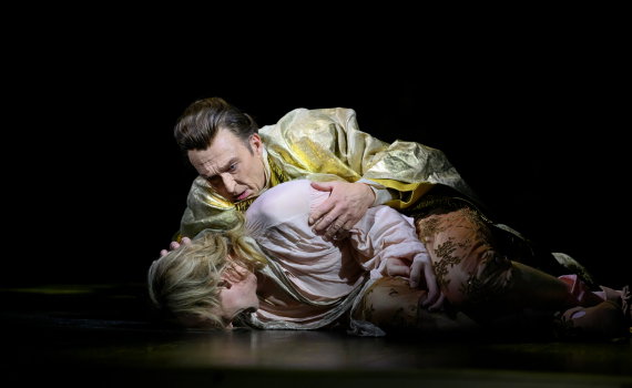 Man i gul 1700-talsrock håller om en annan person i rosa kläder som ligger på golvet.