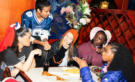 Ungdomar runt ett bord på en pizzeria som äter snabbmat och diskuterar