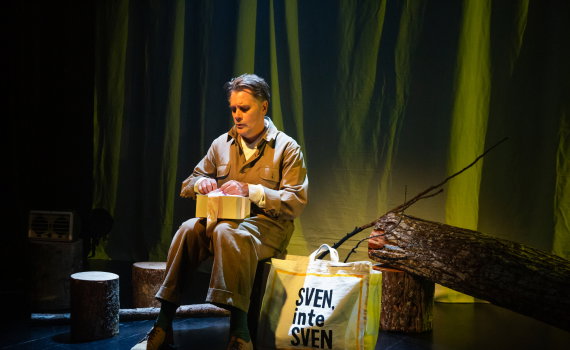 Sven Björklund sitter på en stubbe i ett gröngult ljussatt rum med en kasse bredvid sig som det står Sven, inte Sven på. Han öppnar en fint inslagen låda från ett konditori.