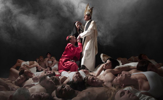 Man i biskopskläder står med nunna och man i röd kåpa; många nakna kroppar ligger runt dem.