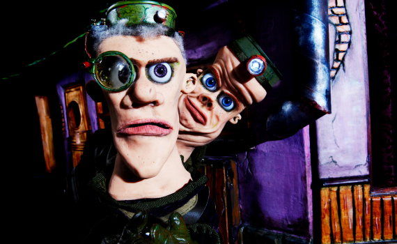 Närbild på två dockfigurer med stora ögon och pannlampor, den ena med förstoringsglas över ena ögat.