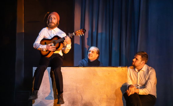 Halvdan i skägg och medeltida mössa som sitter på pianot och spelar gitarr.