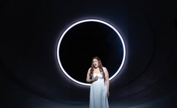 En kvinna sjunger opera på en scen, hon står i en ljuscirkel.