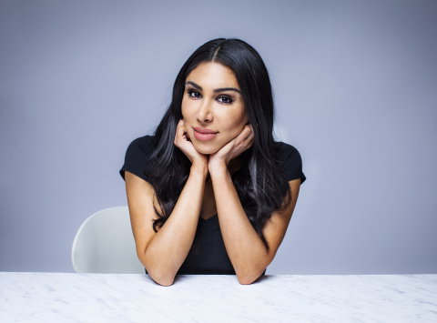 Kvinna i 30-årsåldern med långt mörkt hår sitter vid bord och vilar hakan i händerna.