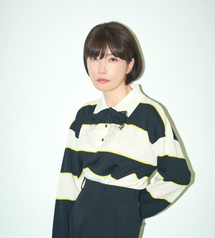 Mieko Kawakami står mot en ljus bakgrund i ett minimalistiskt porträtt med tydliga kontraster och ett lugnt, fokuserat uttryck.