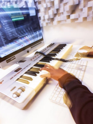 En person sitter vid en dator och jobbar med ett ljudredigeringsprogram.