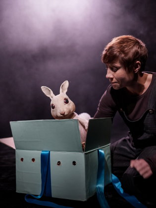 En kvinna tittar på en kanindocka som kommer upp ur en låda. 