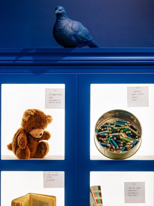 Ett blått skåp med bilder på en nalle, färgkritor, en bok med mera. 