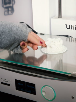 Hand i grå tröja tar bort 3D-printad vit modell från en 3D-skrivare.