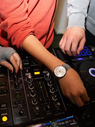 Närbild av tre personers händer som justerar inställningar på en DJ-mixer.