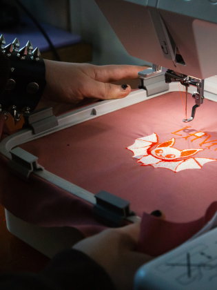 Broderimaskin syr en fladdermusdesign med texten "LAVA" på rosa tyg.