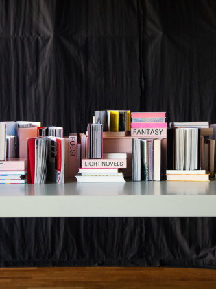 Bord med uppställda böcker i olika genrer som "Konst", "Fantasy" och "Poesi".