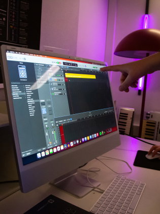 Person pekar på datorskärm med musikprogram i ett rum med lila ljus.