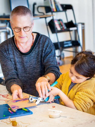 Ett barn och en vuxen sitter vid ett bord och skapar konst av kartong