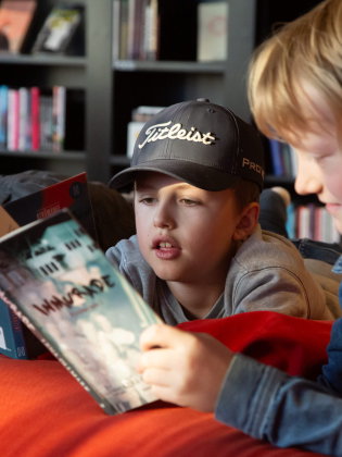 Tre barn läser varsin bok i biblioteket