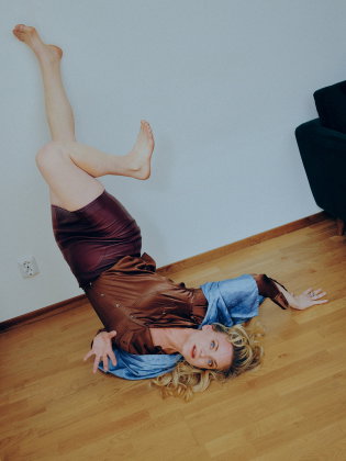 Kvinna i 30–40-årsåldern ligger på golvet med benen upp mot väggen, iklädd brun klänning med blå detaljer.