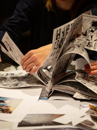 Fyra personer bläddrar i och klipper ut bilder ur serietidningar vid ett bord fullt av papper.