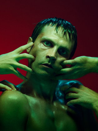 Barbröstad man med blött hår omgiven av flera händer som rör vid hans ansikte och överkropp, mot röd bakgrund.