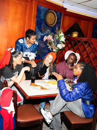 Ungdomar runt ett bord på en pizzeria som äter snabbmat och diskuterar