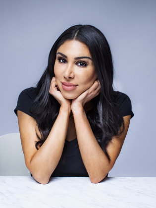 Kvinna i 30-årsåldern med långt mörkt hår sitter vid bord och vilar hakan i händerna.