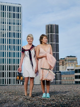 Stina Ekblad och Iiris Viljanen i underkjolar uppe på Kulturhusets tak. I handen håller Stina ett par steppskor och Iiris ett notställ