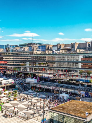 Flygvy över Kulturhuset vid Sergels torg i Stockholm, med många människor på torget och stadsliv i soligt väder.