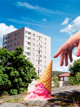 stor hand sträcker sig ner mot en smält glass som ligger upp och ner på en kulle framför ett höghus.
