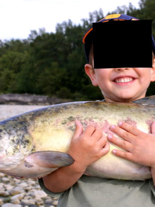 Ett barn står rakt fram och håller upp en stor fisk med båda händerna.