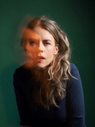 Annika Norlin blickar rakt mot kameran i ett drömskt porträtt med mjuka färger och ett varmt ljusskimmer över ansiktet.